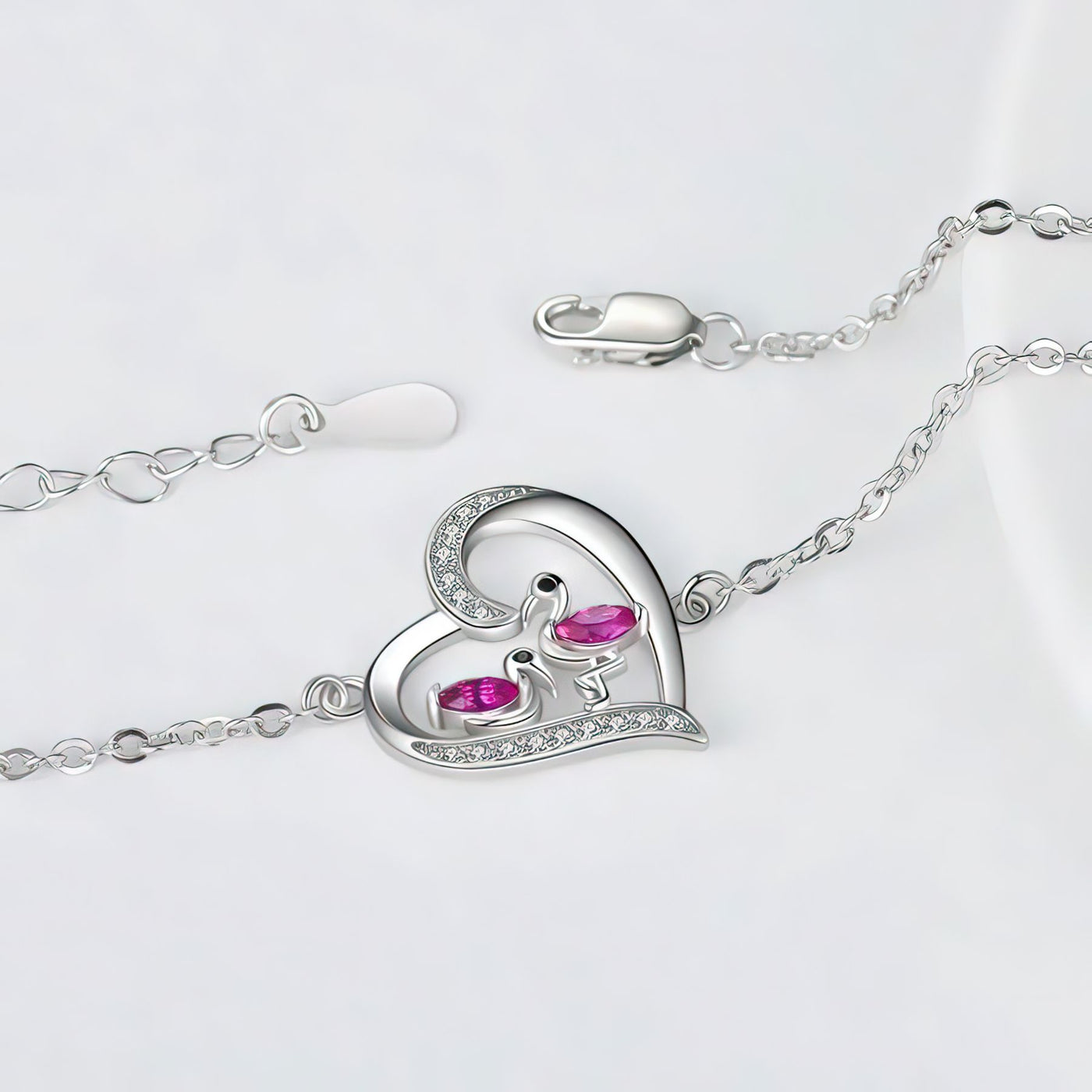 Silver flamingo bracelet with a heart-shaped clasp featuring pink gemstones on a light gray background