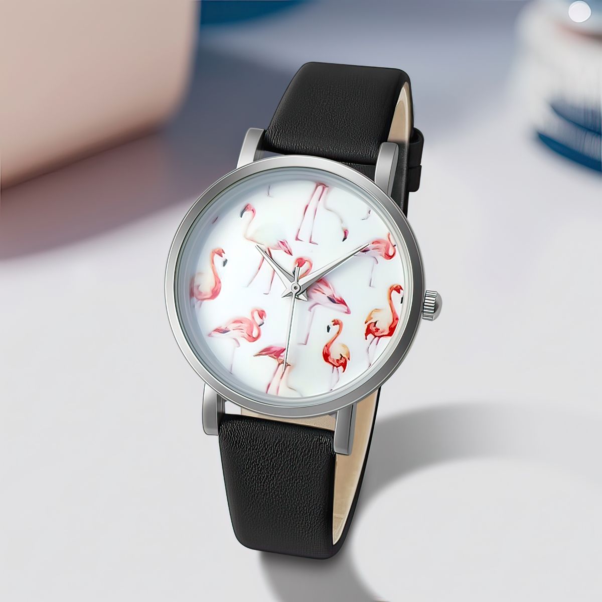 Watch with flamingo design on the dial and black leather strap on a light gray background