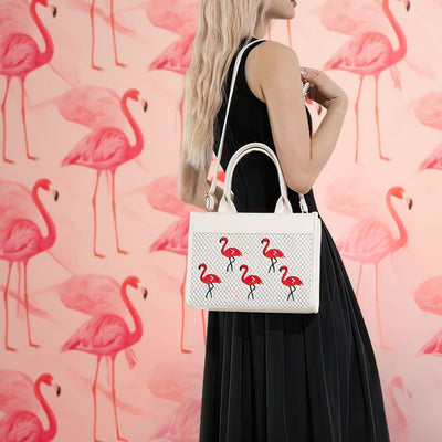 Woman holding a white handbag with flamingo design against a pink flamingo patterned background