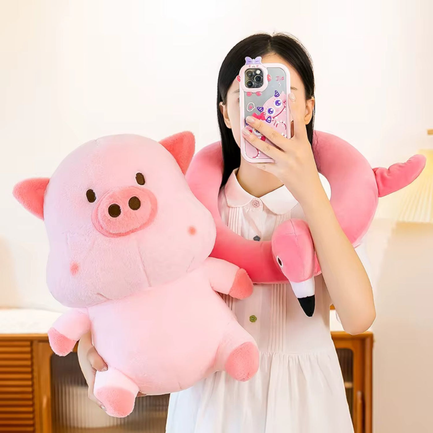 Person holding a pink plush pig toy and a matching inflatable neck pillow.