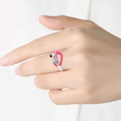 Hand wearing a flamingo-shaped ring with a pink band on a white background