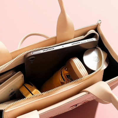 Open beige handbag with phone, sunglasses, and other items on a pink background