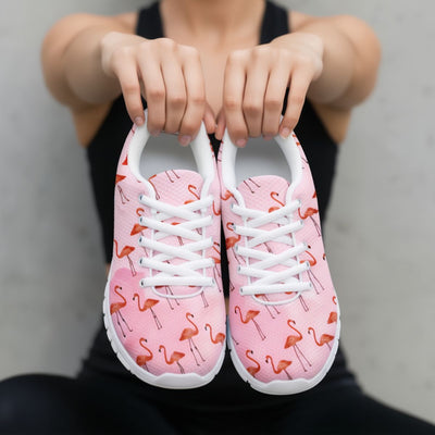 Pink sneakers with flamingo pattern held by a person against a neutral background