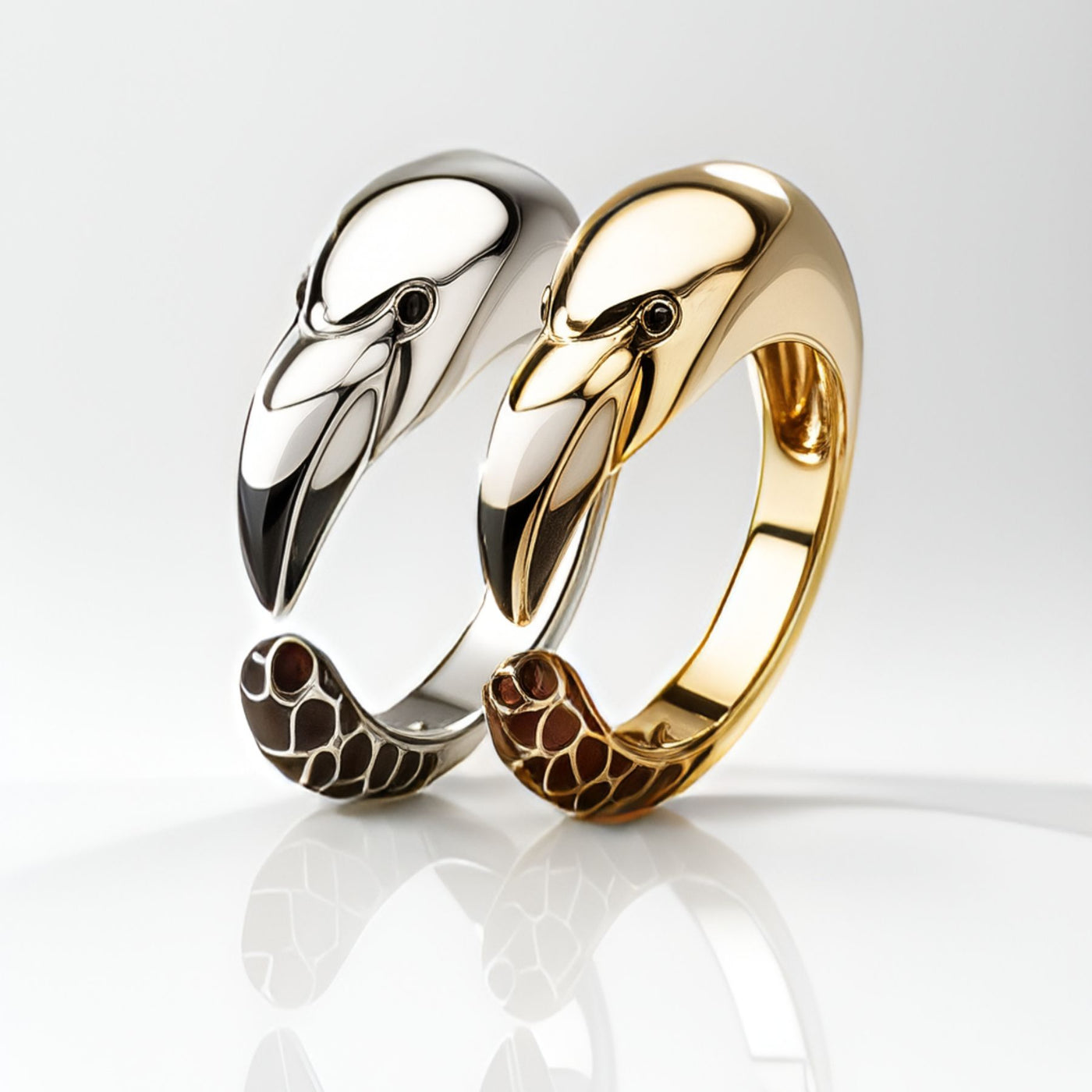 Two flamingo-shaped rings, one gold and one silver, on a reflective surface.